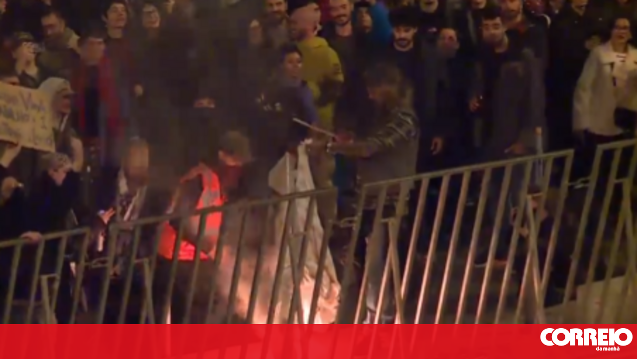 Protesters throw glass bottles and burn flag near the Assembly of the Republic