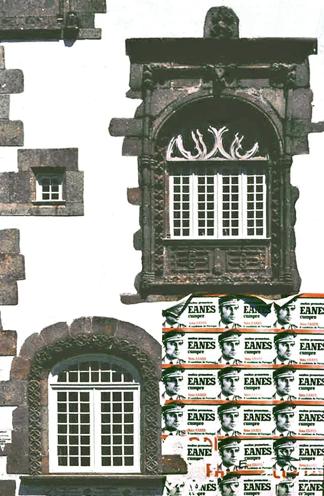 A whitewashed granite house front with two carved stone window frames. Below the upper window, the wall is covered with rows of identical green and white posters showing a man in a military cap beside the word Eanes.