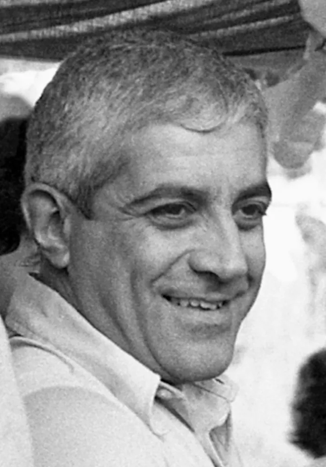 Black-and-white close-up of a smiling man with short greying hair and a light open-necked shirt.