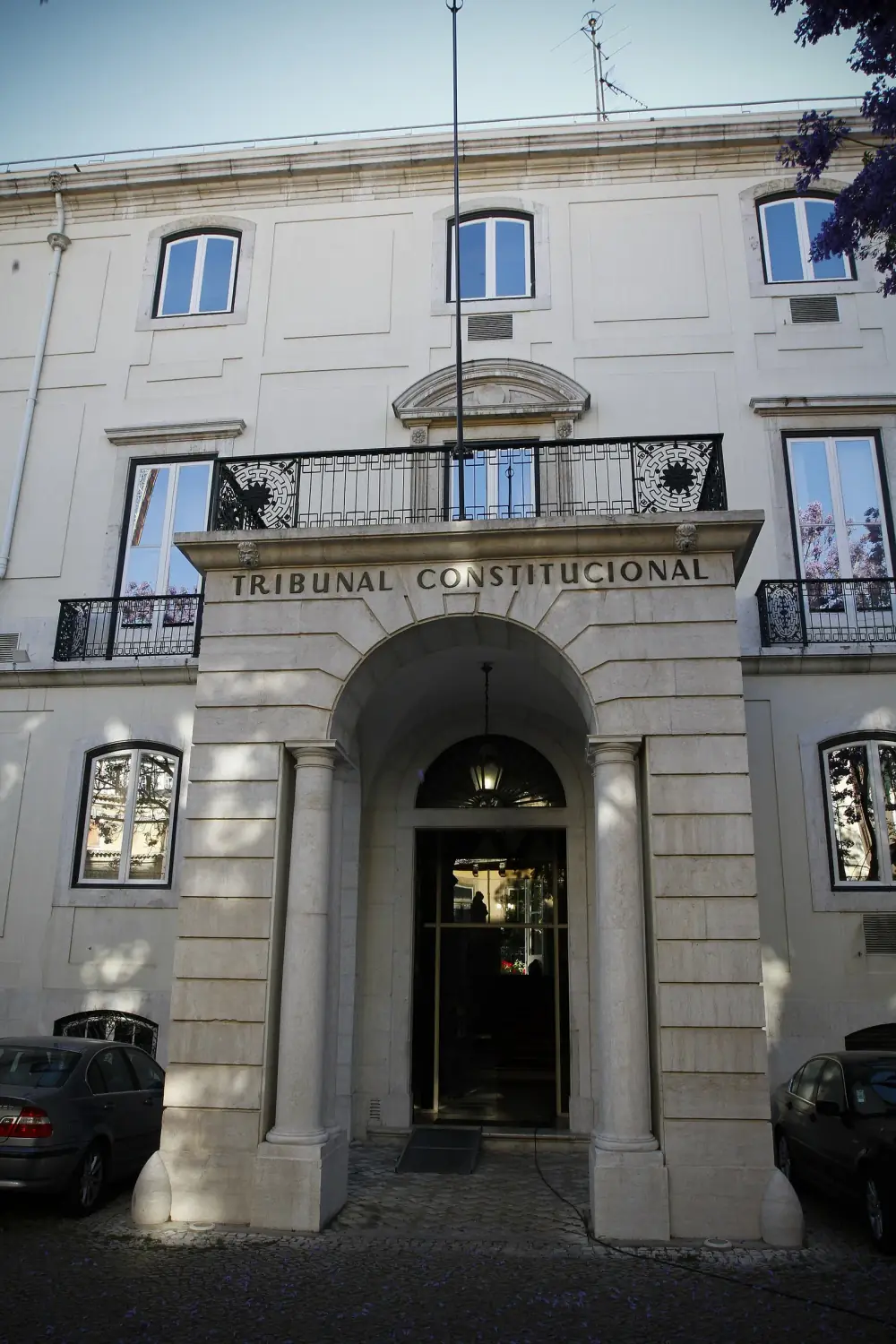 The stone entrance porch of a pale Lisbon townhouse, with two columns, an arched doorway, a balcony above and the words Tribunal Constitucional carved over the arch.