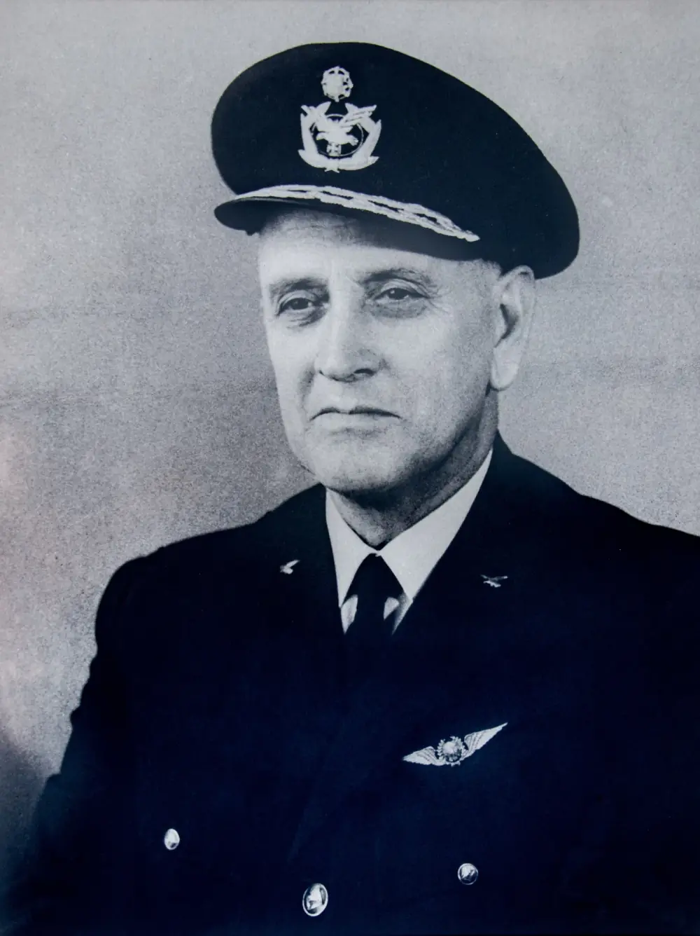Black-and-white portrait of an older man in an air force officer’s dark uniform and peaked cap, with pilot’s wings on his chest.