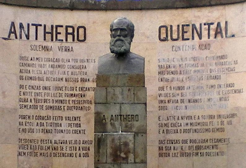A bronze bust of a bearded man on a stone pedestal inscribed A Anthero, in front of a curved stone wall carved with the words Anthero Quental and the full text of two sonnets.