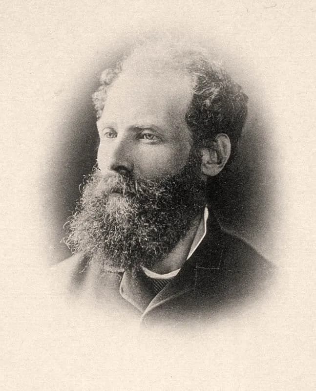Oval-vignetted photograph of a balding man in his forties with curly hair at the sides and a long bushy beard, looking to the left, in a dark jacket.