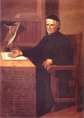 Oil portrait of an elderly, clean-shaven priest in a black cassock and skullcap, seated in a wooden armchair at a desk with a crucifix, a quill in an inkwell and a sheet of paper. A long painted inscription fills the lower left corner.