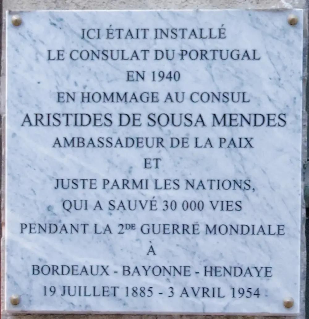 A square white marble plaque fixed to a wall with four brass bolts. Its black capital letters, in French, say the Portuguese consulate was here in 1940 and honour Aristides de Sousa Mendes, Righteous Among the Nations, who saved 30,000 lives at Bordeaux, Bayonne and Hendaye.