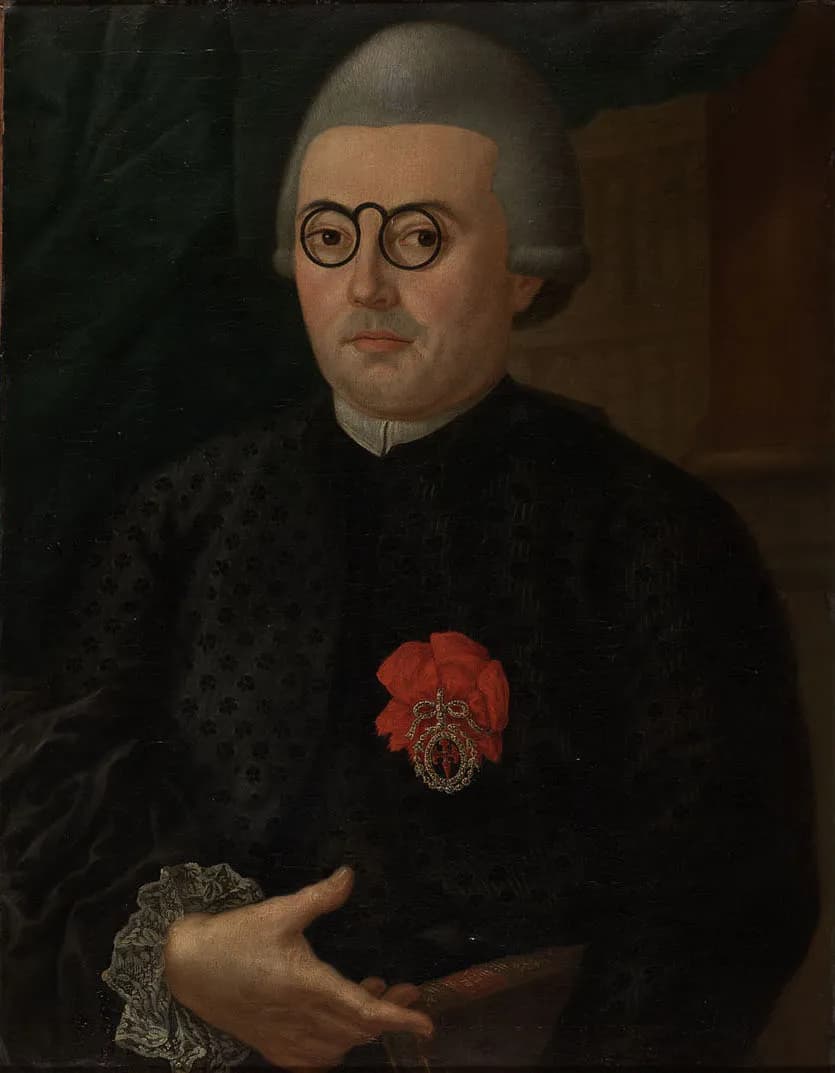 Oil portrait of a heavy-set man in a grey wig and round black-rimmed spectacles, wearing a dark patterned gown with a lace cuff. A red ribbon bow with a jewelled badge is pinned to his chest and he holds a closed book.