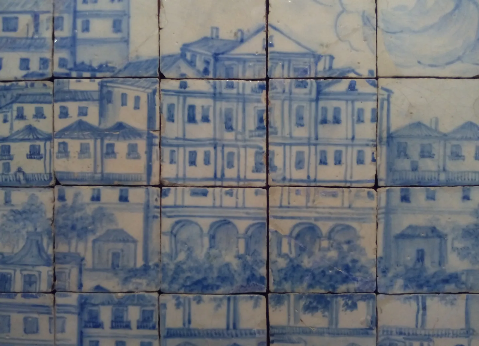 Detail of blue and white glazed tiles painting a large three-storey building with a pediment and an arcaded ground floor, surrounded by smaller houses and trees.