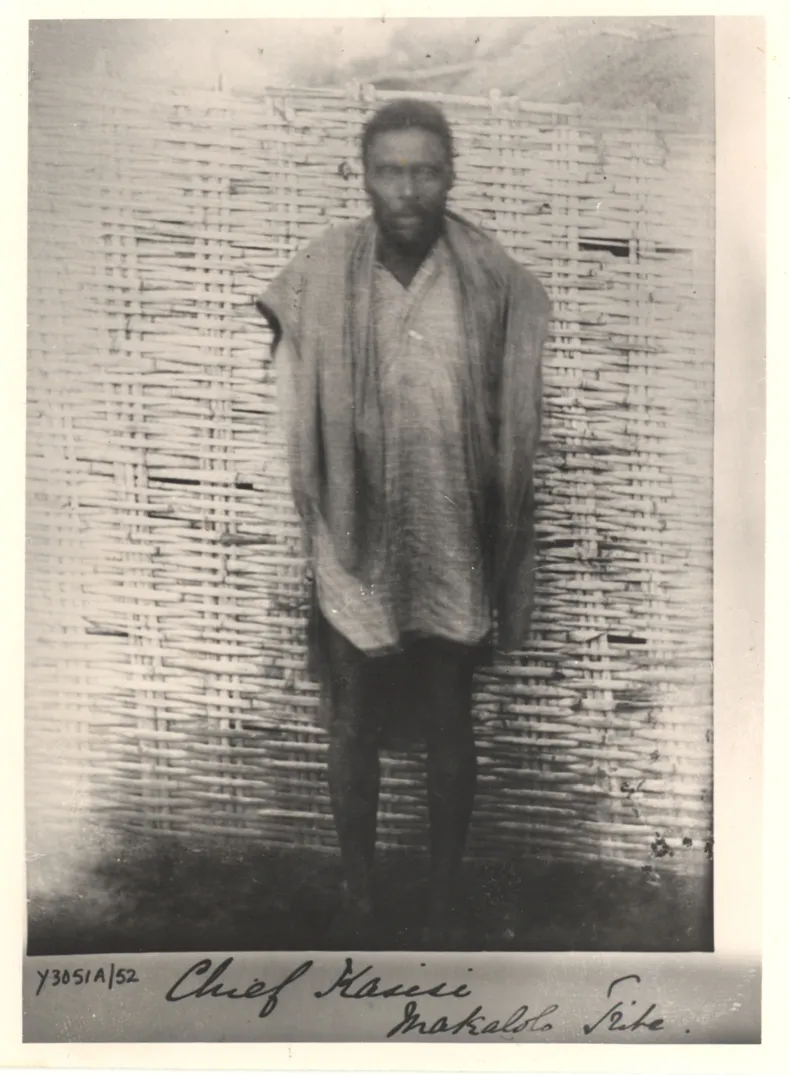 An old black-and-white photograph of a bearded African man standing in front of a woven reed wall, wearing a long shirt with a cloth over his shoulders. A handwritten label below reads Chief Kasisi, Makololo Tribe.