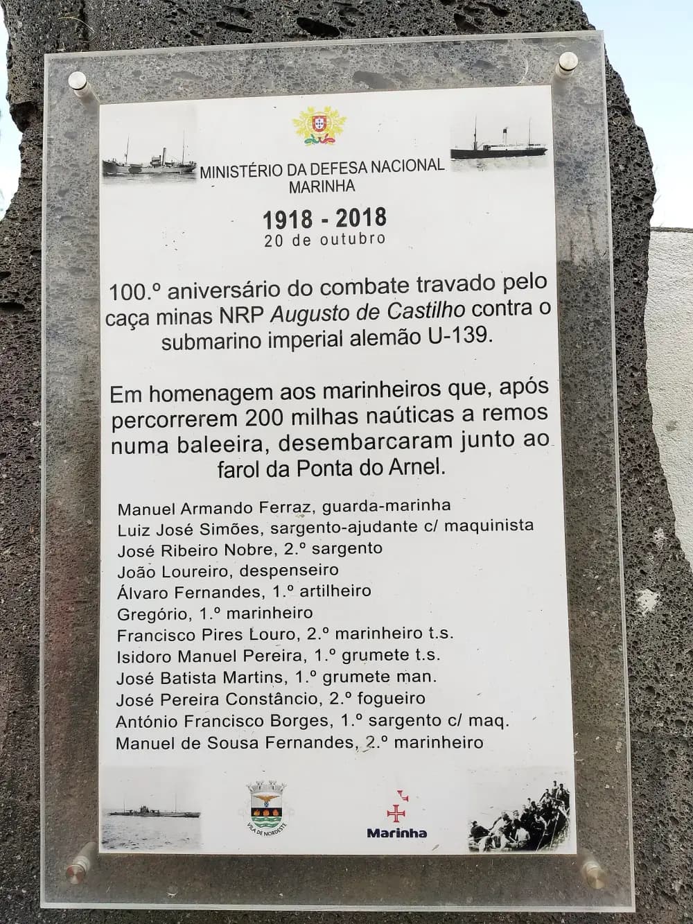Clear acrylic plaque on a dark volcanic stone, with the national coat of arms, small photographs of two steamers, a submarine and men in a crowded boat, and a list of twelve names with ranks.