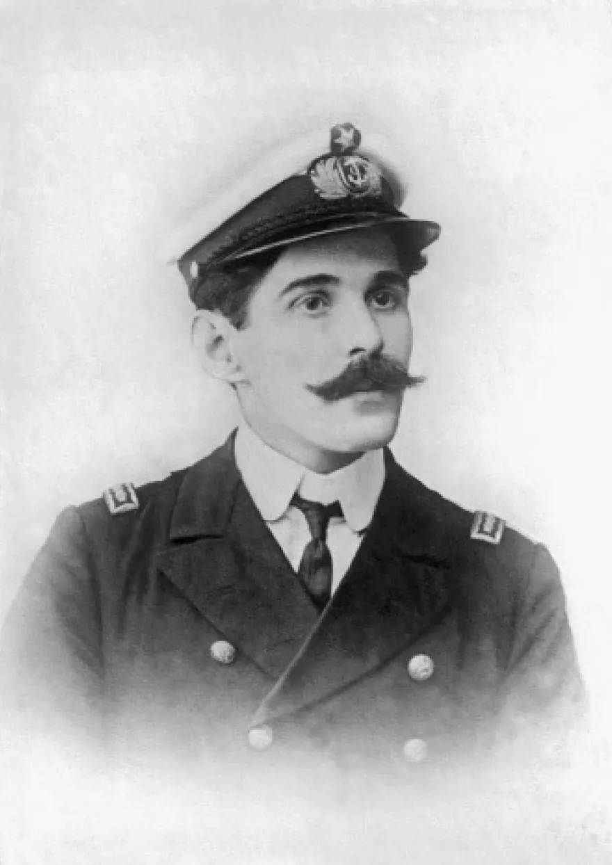 Head-and-shoulders portrait of a young man with a thick moustache, wearing a naval officer's peaked cap with a badge and a double-breasted jacket with collar insignia.