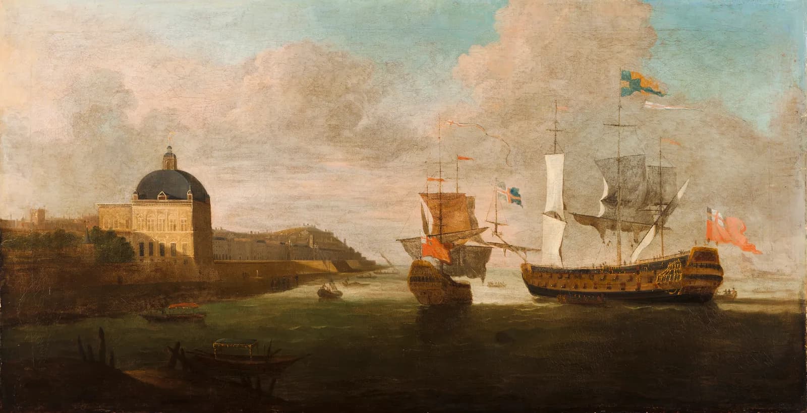 An oil painting of a wide river under a cloudy sky. On the left bank stands a pale palace with a large dark dome, with a long line of buildings behind it; in the middle of the river two tall sailing warships, one flying a large red ensign, ride at anchor among small boats.