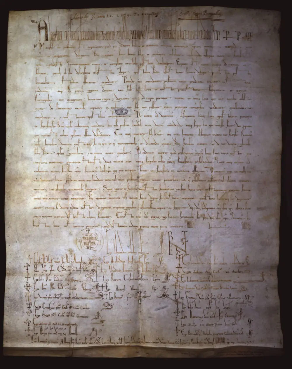 A sheet of aged parchment covered in dense lines of medieval Latin script, with a round papal sign and a large monogram near the foot, above columns of signatures.