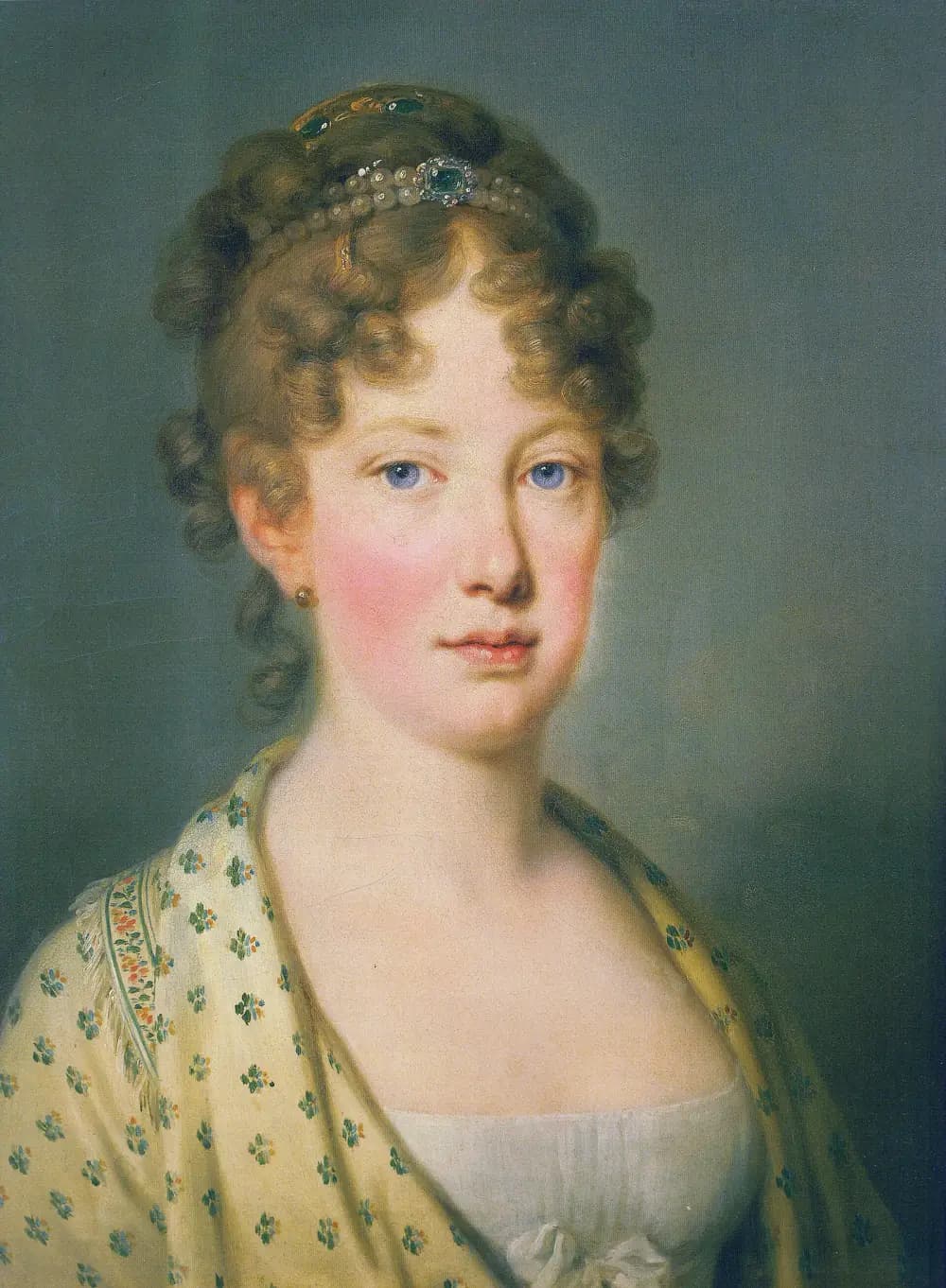 Head-and-shoulders portrait of a young woman with fair curled hair held by a band of pearls and a green jewel, blue eyes and flushed cheeks, wearing a white dress and a cream shawl patterned with small green and red flowers.