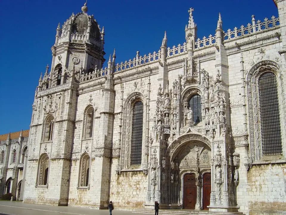 The richly carved south front of a white limestone monastery, with a domed tower, rows of pinnacles and an elaborate central doorway.