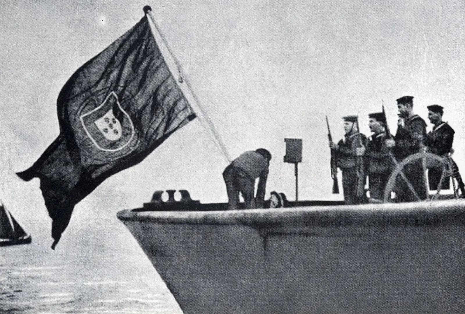 The Portuguese flag with its coat of arms flies from the stern of a steamer; a man bends over the deck while four sailors with rifles stand to attention by the wheel.