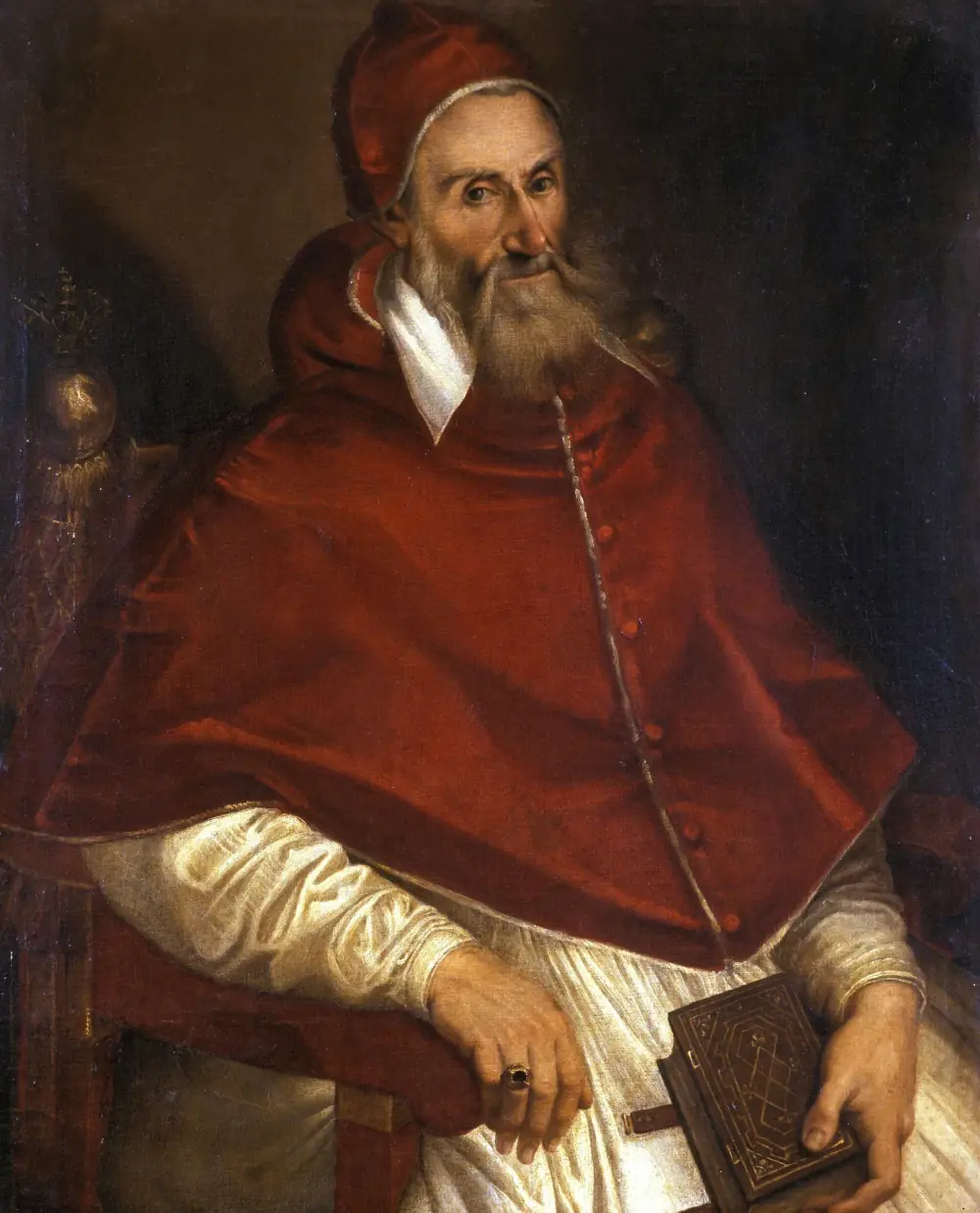 Half-length portrait of an old man with a long grey beard, seated in an armchair. He wears a red cap and a red cape buttoned down the front over a white robe, and holds a closed book with a tooled leather cover on his lap. A ring is on his right hand, and a gilded finial of the chair shows behind his shoulder.