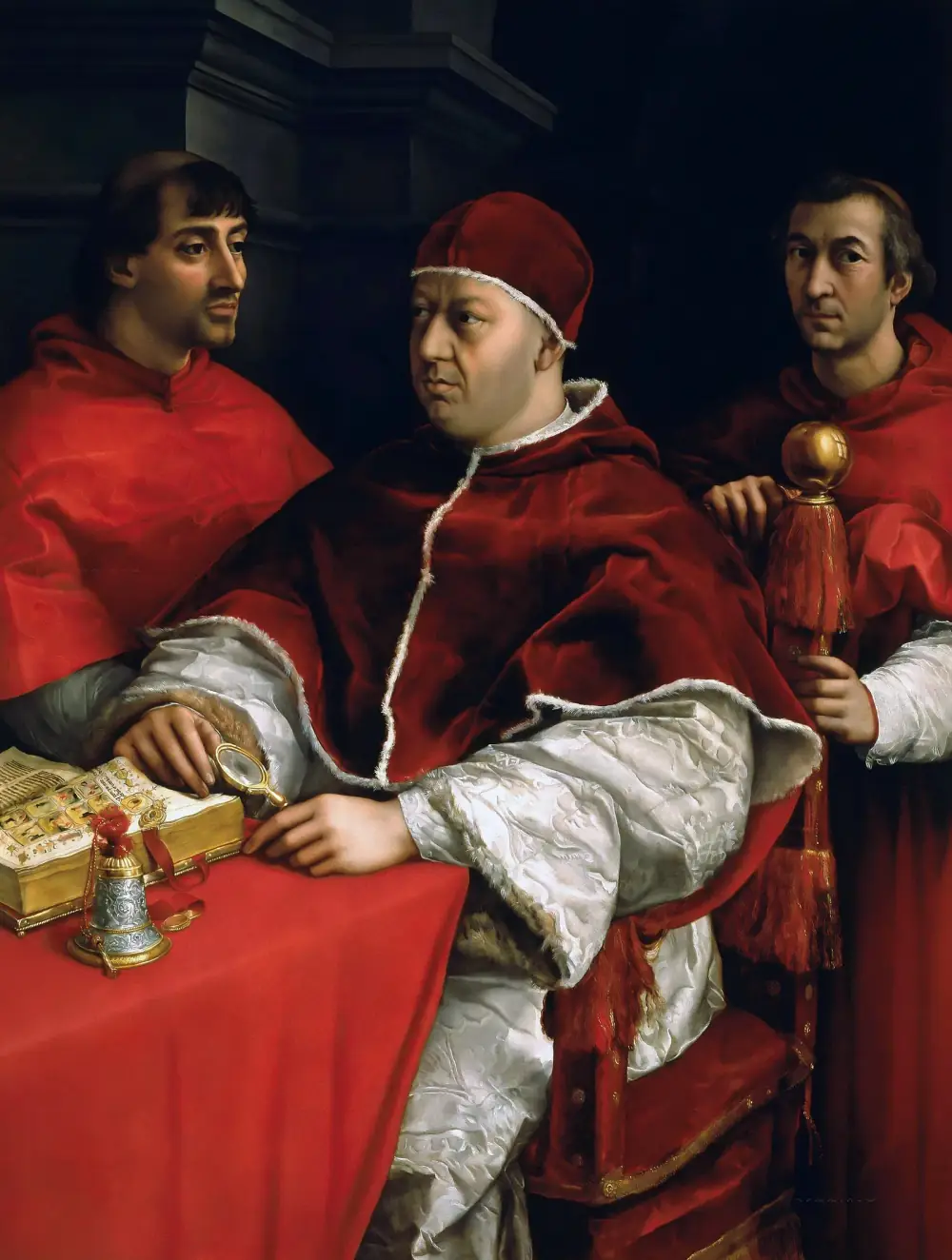 A heavy-set man in a red velvet cap and cape over a white damask robe sits at a table covered in red cloth, holding a magnifying glass over an illuminated book beside a silver bell. Two men in red cardinal's robes stand behind him, one holding the back of his chair.