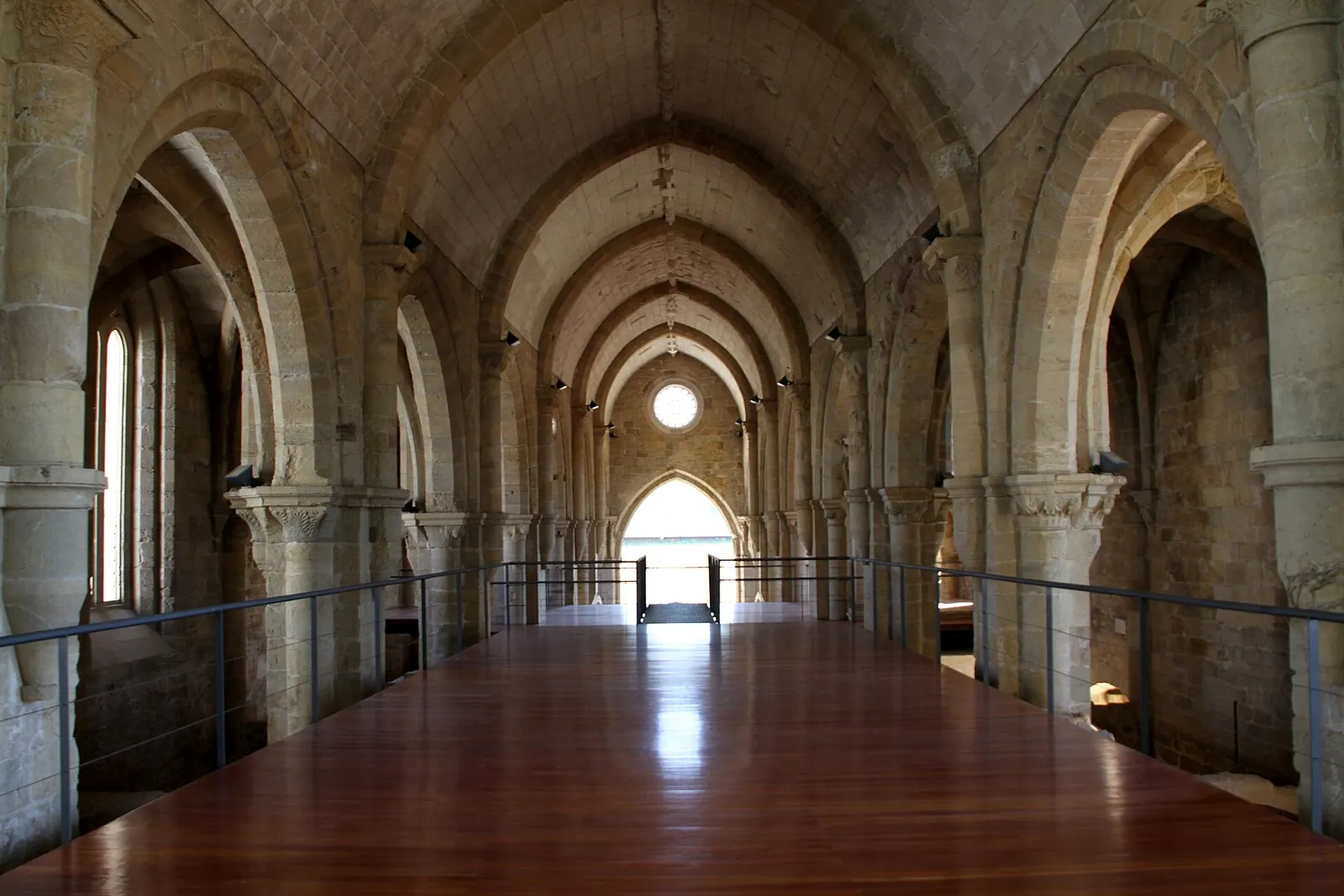 A long Gothic nave of pale stone with rows of round columns and pointed arches, a wooden floor and a round window at the far end letting in light.