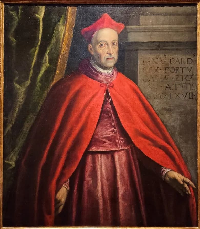 Painted portrait of an old, clean-shaven man in a red biretta and a long red cape over crimson robes, in front of a green curtain and a stone pedestal carved with a Latin inscription.