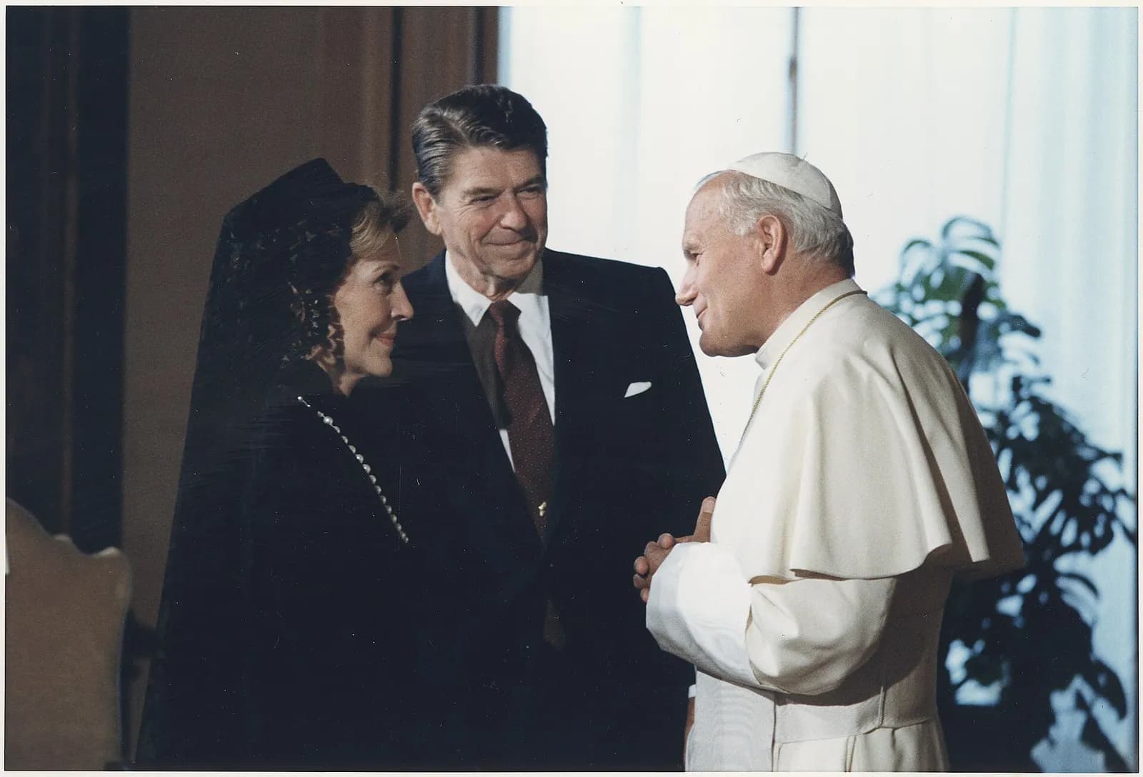 John Paul II, in a white cassock and skullcap, smiles as he talks with Ronald Reagan, in a dark suit, and Nancy Reagan, in a black dress and black lace veil, in a room at the Vatican.