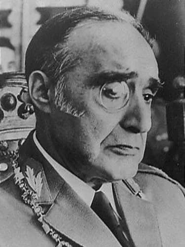 Black-and-white head-and-shoulders portrait of an older, balding man in army uniform with embroidered collar insignia, wearing a monocle and looking to one side.