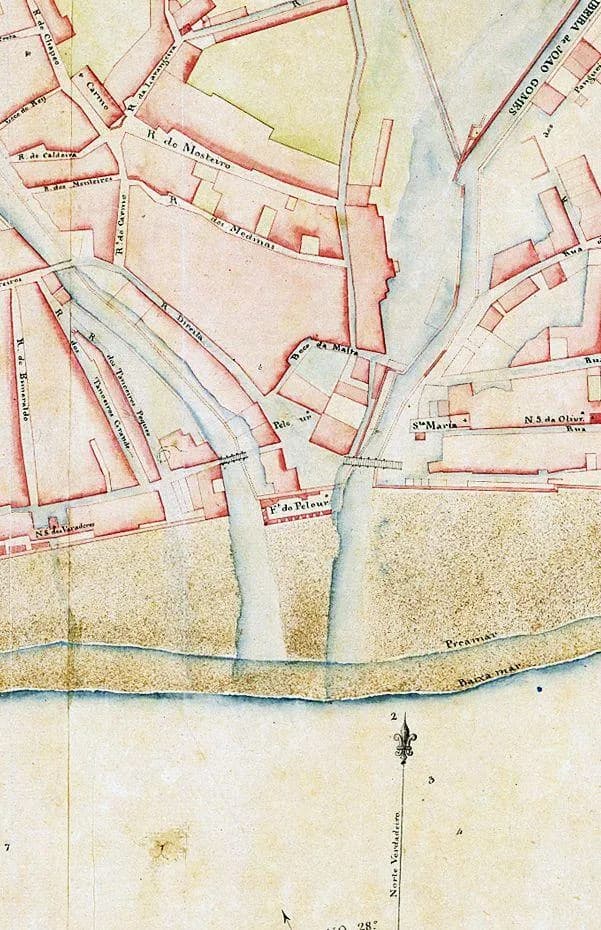 Detail of a hand-coloured plan of a seafront town. Pink blocks of buildings and named streets are crossed by two pale blue watercourses that run down to a sandy beach and the sea.