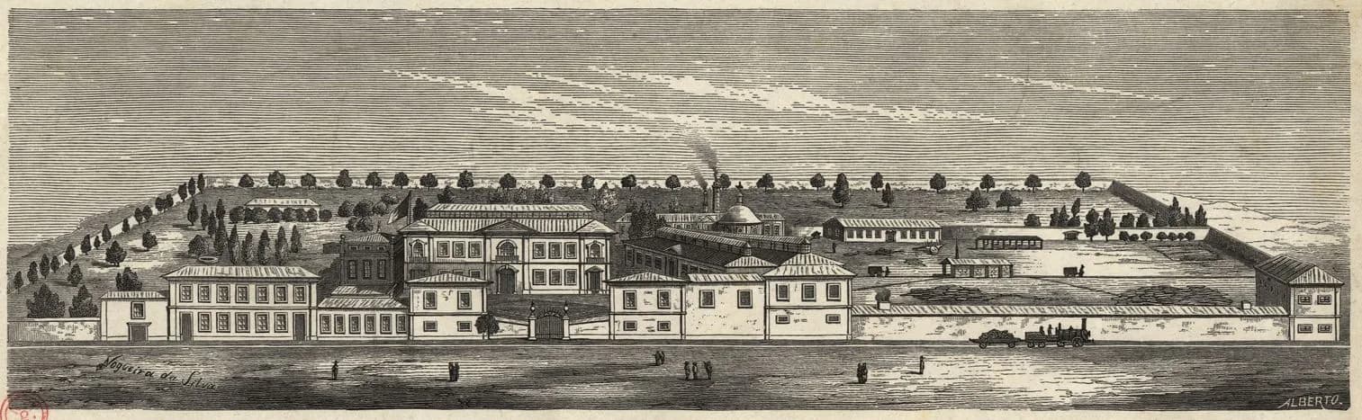 A wide engraved view of a large walled industrial complex: two-storey buildings with many windows along a road, a palatial block with a central pediment behind them, long workshop sheds, a domed kiln with a smoking chimney and a small steam train running beside the outer wall. Pine trees line the slopes behind.