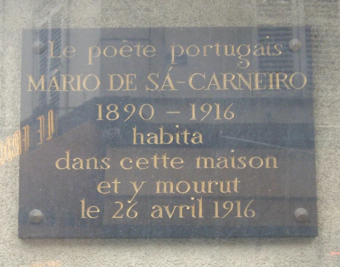 A dark polished stone plaque with gold lettering, partly reflecting the street, reading in French that the Portuguese poet Mário de Sá-Carneiro, 1890 to 1916, lived in this house and died here on 26 April 1916.