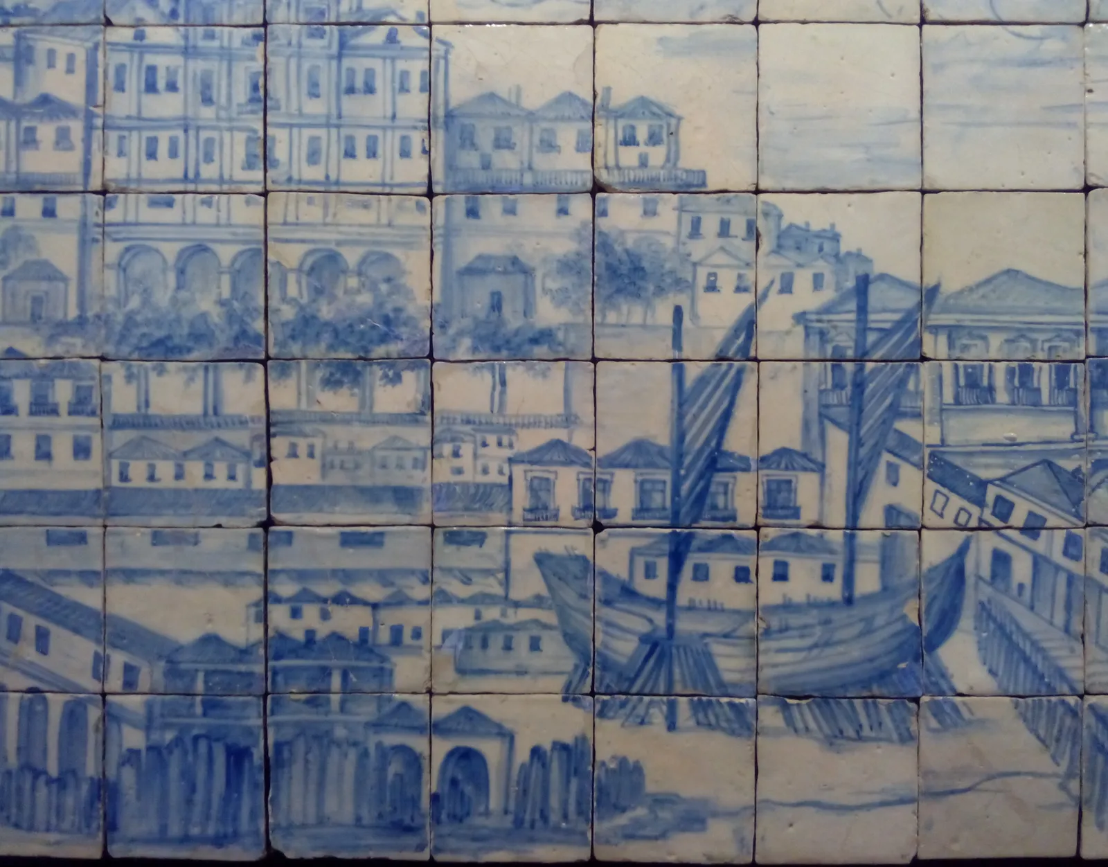 Blue and white glazed tiles showing a waterfront of tall houses and arcades, with a large ship propped on timbers on a slipway in the foreground.