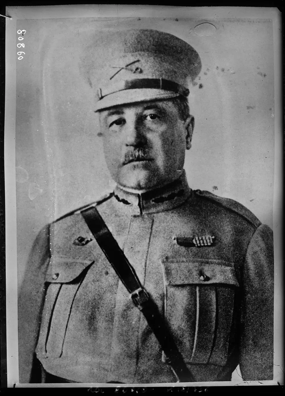 A head-and-shoulders portrait of a man in a peaked military cap and uniform with a diagonal leather strap across his chest. He has a moustache and looks straight at the camera. A catalogue number is written in the top corner of the glass negative.