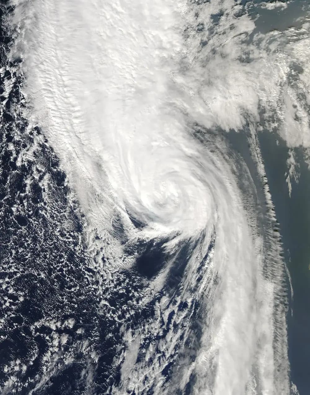 Satellite image of a large comma-shaped swirl of white cloud over the dark blue Atlantic, its centre still tightly wound, trailing a long band of cloud to the south.