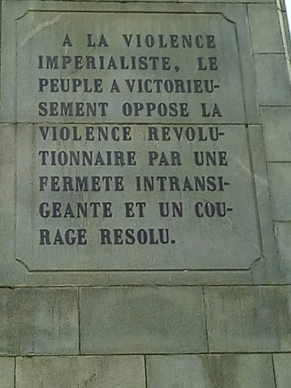A stone panel on a plinth carved in capital letters with a French inscription about the people's victory over imperialist violence.
