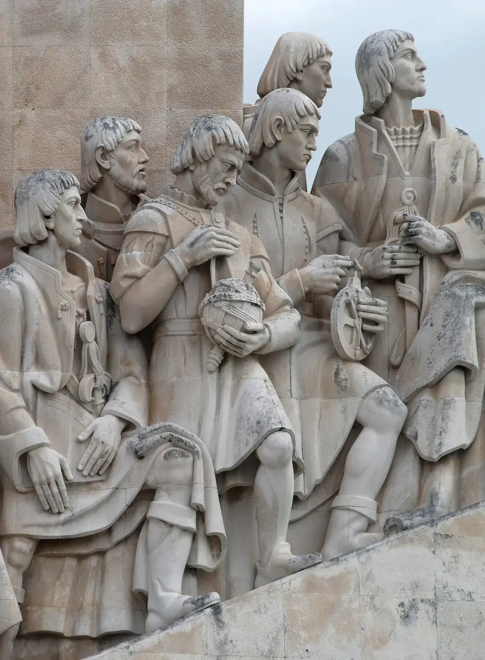 Stone figures in sixteenth-century dress carved on the side of a monument. A bearded man near the centre holds an armillary sphere, a model of the heavens made of rings, and a pair of compasses, while the men around him hold an astrolabe and other navigation instruments.