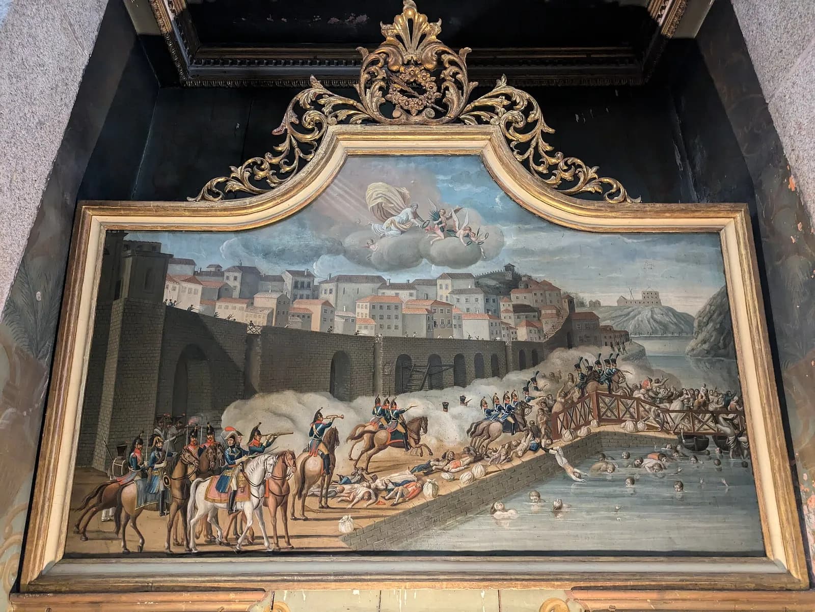 A painting in a gilded frame shows French cavalry and officers on a riverside quay below a walled town. Bodies lie on the quay, people crowd onto a wooden bridge on the right and many more struggle in the water. A robed figure and cherubs appear in the clouds above.