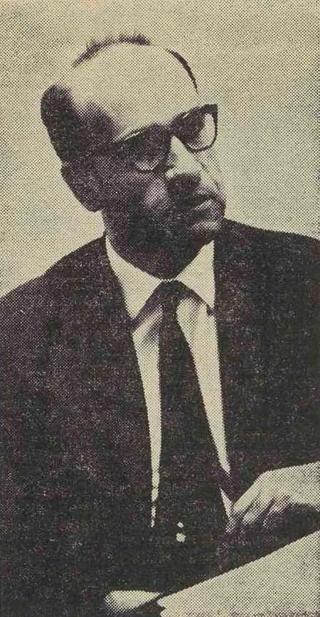 Newspaper halftone portrait of a balding man in thick-framed glasses, white shirt and dark tie, holding papers.