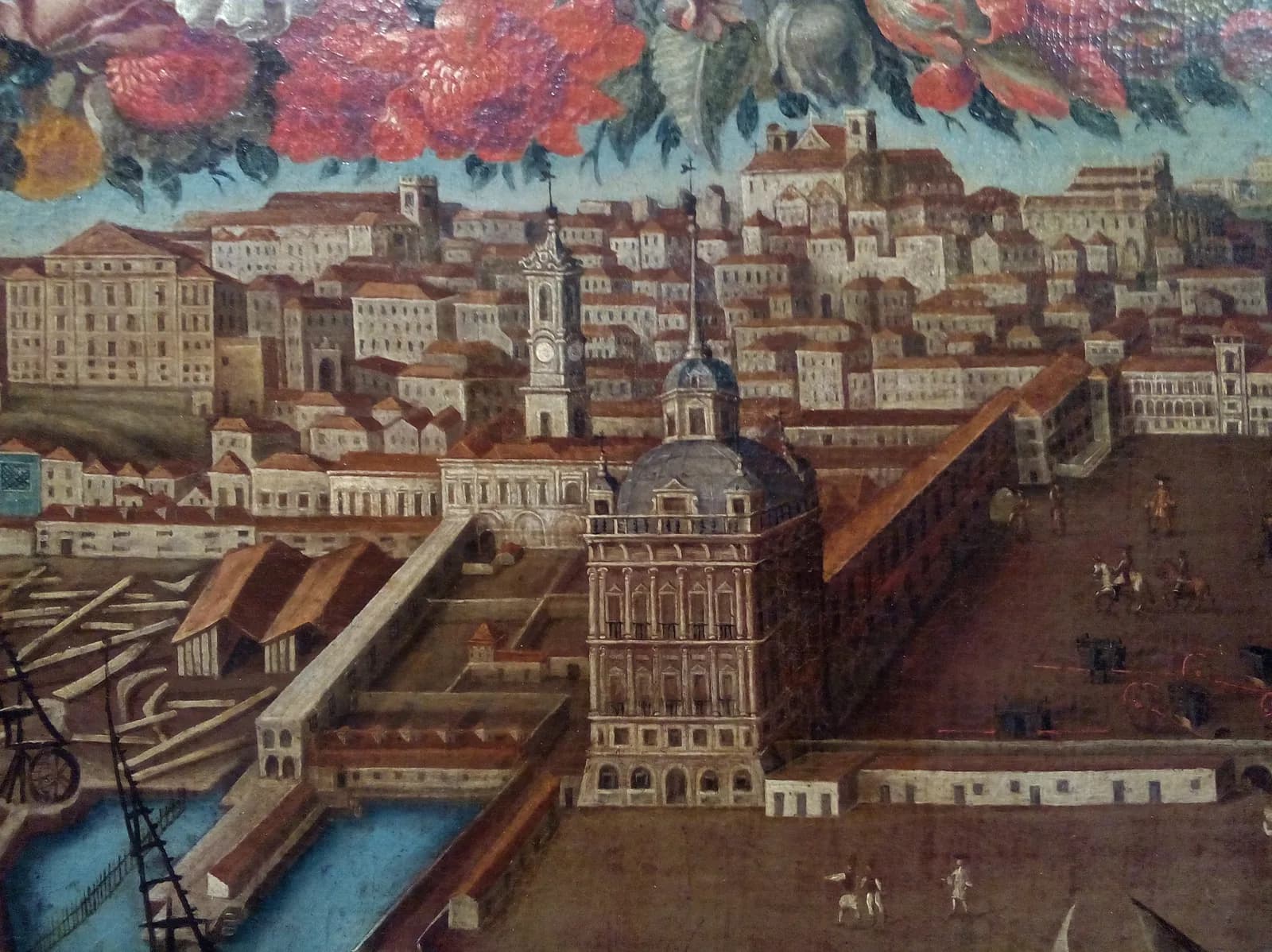 A painted view of Lisbon's waterfront: a tall square palace tower with a grey dome stands at the corner of a long riverside wing and a large open square with riders and carriages, with the hillside city of white houses and church towers behind and a painted garland of red flowers across the top.