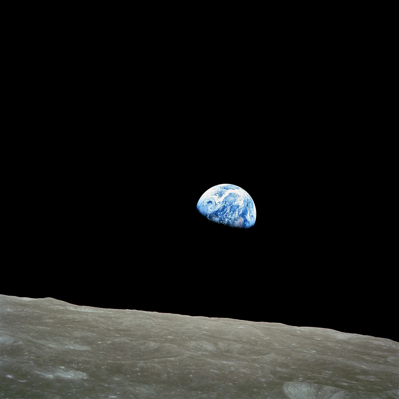 The blue and white Earth, half in shadow, hangs in a black sky above the grey, cratered horizon of the Moon.