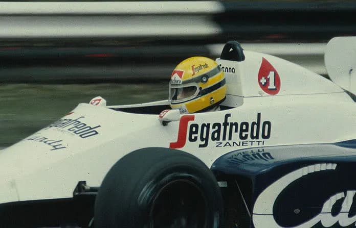 Close view of a white Toleman Formula One car carrying Segafredo sponsorship, its driver wearing a yellow helmet with green and blue stripes.