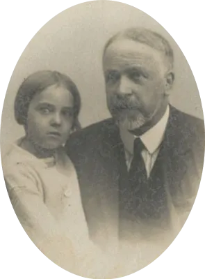 An oval studio portrait of a small girl with a fringe and a pale dress, leaning against a bearded, grey-haired man in a dark suit and tie.
