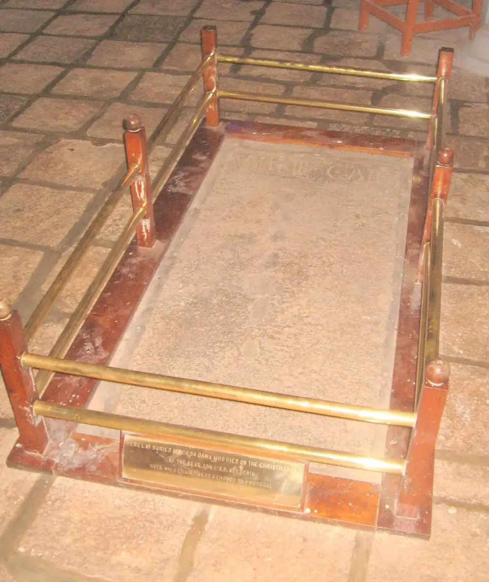 A worn rectangular stone slab set in a church floor, enclosed by a low rail of brass bars on wooden posts, with a small brass plaque at its foot.